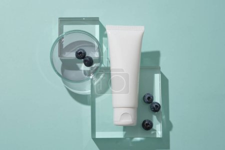 Photo for Top view of cosmetics tube mockup for design placed on transparent podiums, blueberries and essence on petri dish display on blue background. Scene for promote cosmetic, copy space - Royalty Free Image
