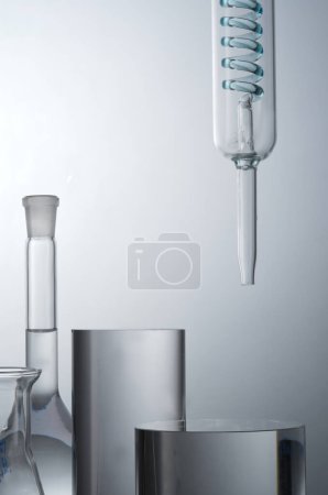 Closeup view of lab glassware filled transparent solution and cylinder podiums for cosmetic product presentation on light background. Concept: research, biochemistry, nature, pharmaceutical medicine