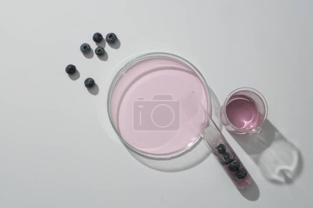 Advertising photo for cosmetic from blueberry extract with fresh blueberries and lab glassware containing purple essence decorated on white background. Natural cosmetic concept