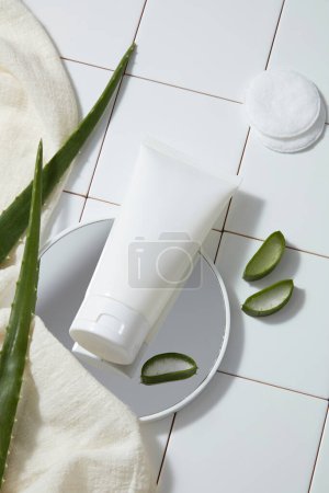 Photo for White plastic tubes unlabeled mockup for cleanser, fresh aloe vera leaves, makeup remover cotton and towel on white tile floor. Bathroom concept, scene for advertising cosmetic of natural extract. - Royalty Free Image
