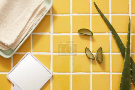 Photo for Advertising photo with copy space for cosmetic of aloe vera extract - fresh aloe vera leaves and slices, mirror and beige towel on yellow tile background. Lifestyle concept, natural ingredient - Royalty Free Image