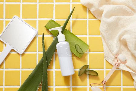 Photo for An unlabeled pump bottle on yellow tile background with fresh aloe vera mirror and beige towel. Mockup for cosmetics of aloe vera extract with lifestyle concept. Space for design - Royalty Free Image