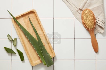 Photo for Scene for advertising cosmetic with aloe vera ingredient - fresh aloe vera on wooden dishes, wooden comb and towel decorated on white tile background. Cosmetics with natural extracts for body and face - Royalty Free Image