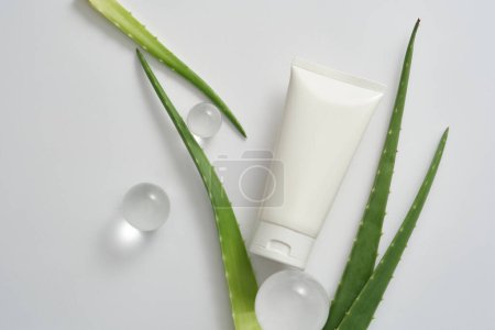 Blank background for branding and minimal presentation - white plastic bottle unbranded with glass balls and fresh aloe vera leaves decorated on white background. Space for design. Top view
