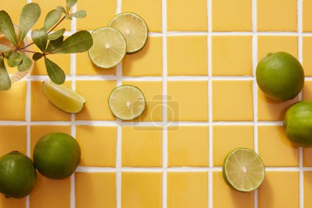 Photo for Beauty frame for advertising cosmetic product with limes and green leaves decorated on yellow tile background. Lime extract contains a lot of vitamin C and nutrients for effective skin care. - Royalty Free Image