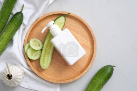 Mockup scene for cleansing and moisturizing cosmetics of cucumber extract. A white pump bottle unlabeled and cucumber slices on wooden dishes, reed diffuser and towel on white background. Copy space.
