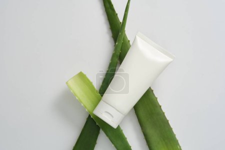 Verjüngende und feuchtigkeitsspendende Kosmetik mit natürlichem Aloe-Extrakt zur Gesichtspflege auf weißem Hintergrund mit frischen Aloe-Vera-Blättern. Attrappe mit weißem Plastikschlauch ohne Beschriftung.