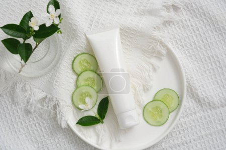Photo for Mockup scene for cosmetic of cucumber extract. Plastic tube, cucumber slices and flower branch on fabric background. Oil-reducing and acne-prevention cosmetics that moisturize and clean the skin - Royalty Free Image