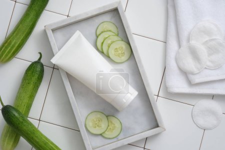 Photo for Advertising scene: cucumber slices, white plastic tube unlabeled, towel and cotton pads on tile background. Mockup for cleansing and moisturizing cosmetics with natural organic ingredients - Royalty Free Image