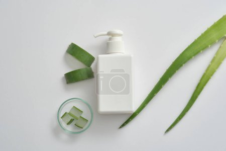 Fresh aloe vera leaves and slices in petri dish on white background with white pump bottle unlabeled. Mockup for cosmetic, cleanser or lotion with aloe vera extract. Space for design