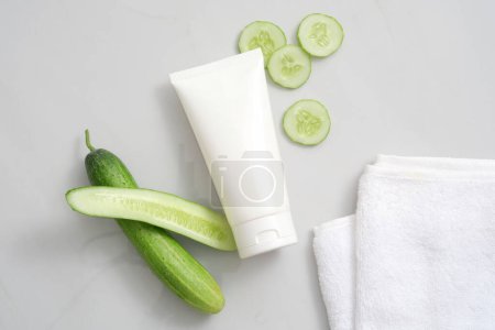 Photo for Top view of white plastic tube unbranded, cucumber sliced and towel on white background. Mockup for product of natural extract, cleansing and moisturizing cucumber cosmetics. - Royalty Free Image