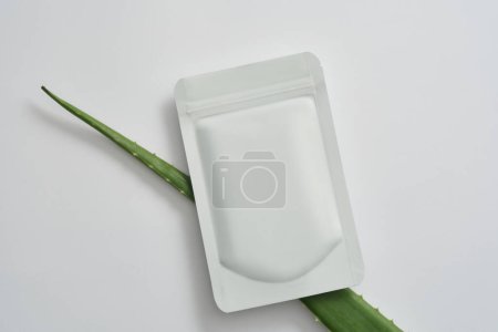 Mockup of a facial sheet mask and aloe vera leaves for cosmetics advertising on a white background. Aloe vera has an anti-aging, wrinkle-preventing, and collagen-stimulating impact.