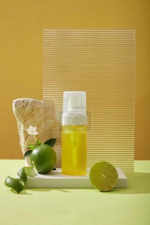 Front view of yellow spray bottle unlabeled on podium, halves of lime, peel, flower, rock and acrylic sheet on yellow background. Mockup scene for product of natural extract - rich in vitamin C.