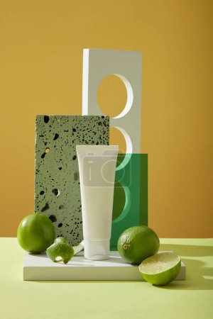 Scene of bottle unlabeled on podium, fresh limes, gray brick and geometric object on yellow background. Mockup for facial cleanser extracted from limes to strengthen, support facial cleansing