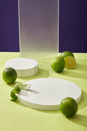 Round empty podium, acrylic sheet and fresh lime citrus (Citrus aurantifolia) on color background. Platform for display cosmetic of lime extract. Minimal concept, front view.