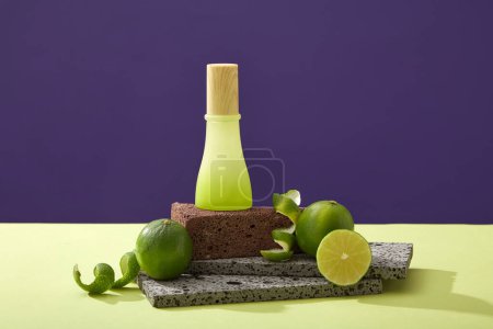 Glass bottle unlabeled on stone podium, halves of lime and spiral peel on color background. Mockup scene for cosmetic of lime extract - rich in vitamin C and nutrients for effective skin care