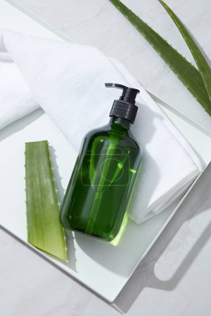 Photo for Top view of green plastic bottle unlabeled placed on white tray with towel and fresh aloe vera leaves on white background. Mockup for facial cleanser or shampoo product extracted from aloe vera. - Royalty Free Image