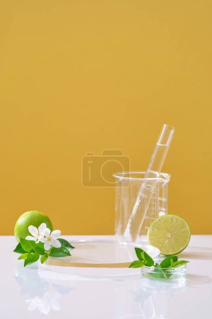 Scene for the display cosmetic with fresh limes, flower and leaves on yellow background and lab glassware. Lime extract is rich in minerals and vitamin C for good skin care.