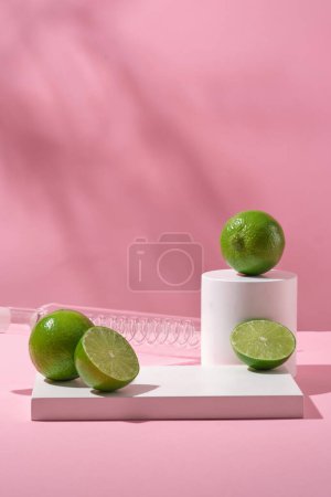 Pedestal for cosmetic product display presentation with white podiums and fresh limes on pink background with natural shadow leaves. Minimal concept for advertising cosmetic of lime extract.
