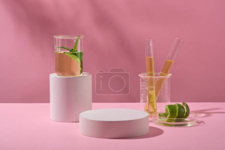 Stage showcase cosmetics on round podium and laboratory equipment containing yellow liquid and peel limes on pink background. Minimal concept.