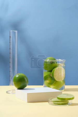 Photo for Minimal background with blank space for display cosmetic of lime extract. White empty podium, fresh limes in beaker and petri dish on blue background with natural shadow leaves. Copy space - Royalty Free Image