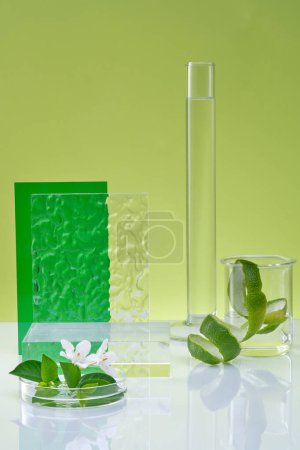 Front view of lab glassware, spiral lime peel and white flower, green leaves on green background. Empty podium for display cosmetic of lime extract. Research and production of natural cosmetics