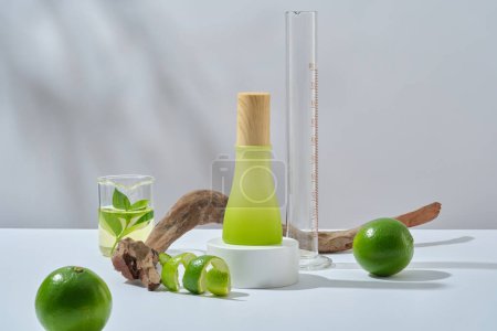 Mockup for product with lime ingredients - glass bottle unlabeled on podium, fresh limes, dried twig and lab glassware decorated on white background with natural shadow leaves. Space for design