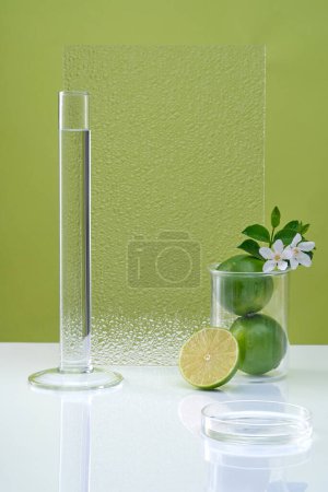 Blank minimal background with lab glassware, fresh lime and flower decorated on green background. Empty space for cosmetic product with ingredient from lime presentation. Copy space.
