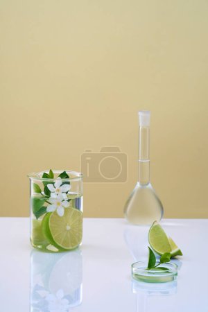 Scene for advertising cosmetic with laboratory concept. Fresh lime slices, leaves and flower in beaker, volumetric flask and petri dish filled transparent liquid. Empty space for product presentation