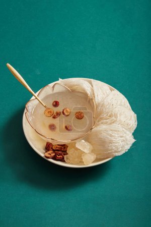 Close up of bowl soup, bird nest, rock sugar and jujube are on white dishes, isolated on green background. Bird nest is one of most important supplements for longevity and youth.