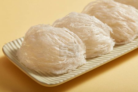 Close up of some raw bird's nests are arranged on a white long rectangular plate, on beige background. Food of natural origin, expensive culinary ingredient for health.