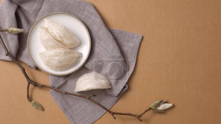 Photo for Healthcare food with Edible bird's nest raw on round dishes, gray handkerchief and flower branch on brown background. Space for text and design. Top view, flat lay. - Royalty Free Image