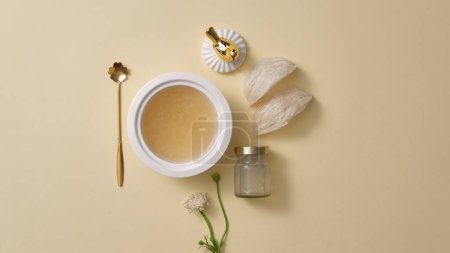 Foto de Vista superior de un tazón de sopa cocinado del nido de pájaro, una botella de agua del nido de pájaro sin etiquetar en el lateral, sobre un fondo beige. Publicidad foto para el producto. - Imagen libre de derechos