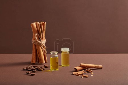 Photo for Scene advertising products with glass bottle containing essential oils, cinnamon sticks and coffee. Herb good for health, heart and anti aging. Cinnamon oil has many uses in skincare and cosmetics - Royalty Free Image
