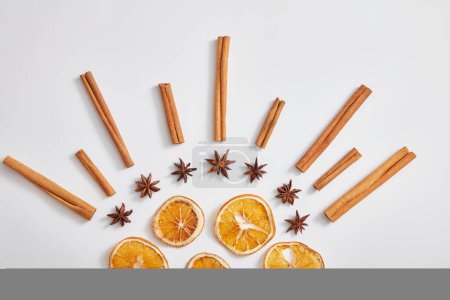 Téléchargez les photos : Bâtonnets de cannelle, anis et tranches d'orange séchées sont disposés dans une forme unique que le soleil sur fond blanc. Concept minimal pour la publicité du produit. Vue de dessus, plan plat. - en image libre de droit