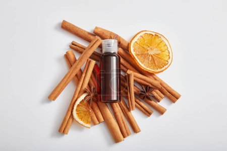 Photo for Mockup since for cosmetic product of herbal extract with brown bottle without label, cinnamon sticks, anise and dried orange slices on white background. Top view, flat lay. - Royalty Free Image