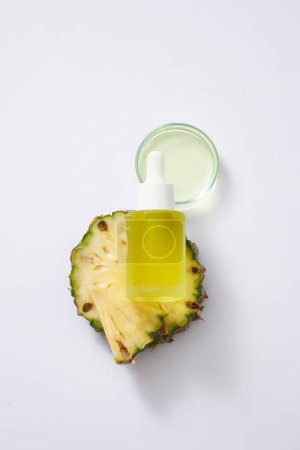Photo for Mockup scene for serum, cosmetic of pineapple extract with glass bottle unlabeled containing yellow essence on fresh pineapple slices and petri dish on white background. Top view, space for design. - Royalty Free Image