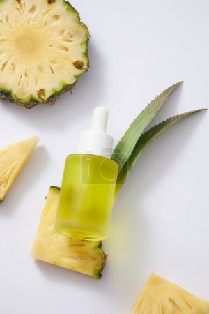 Photo for A glass bottle unlabeled containing yellow liquid with dropper cap, fresh pineapple (Ananas comosus) slices and leaves on white background. Mockup for serum product, from natural extract. Top view. - Royalty Free Image