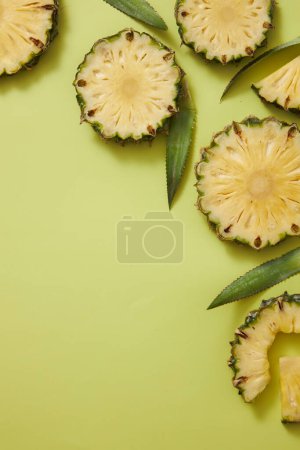 Foto de Marco de rodajas de piña fresca (Ananas comosus) y hojas verdes decoradas sobre fondo verde. Espacio vacío para texto y diseño. Frutas tropicales, vista superior, espacio para copiar - Imagen libre de derechos