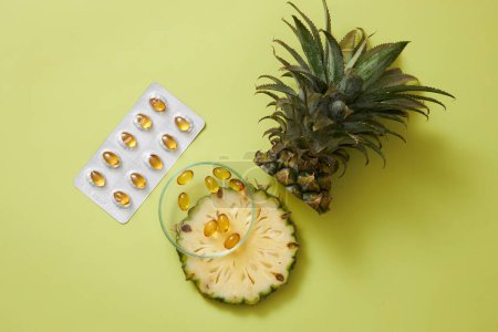 Téléchargez les photos : Ananas frais et capsule douce décorée sur fond vert. Scène publicitaire pour un produit extrait de l'ananas, riche en vitamines et bon pour la beauté. - en image libre de droit