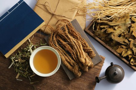 Angelica sinensis roots on a rectangular tray, medicine cup, blue book, medicine package and some dries herb on light background. Scene for advertising, photography traditional medicine content