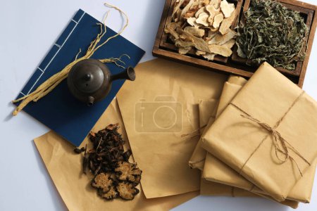 Scene for advertising traditional Chinese medicine with dried herbs on wooden tray, book and medicine package on light background. Top view, copy space
