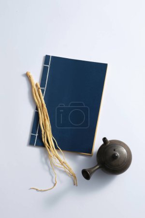 Téléchargez les photos : Quelques racines de pilose asiabell sur le livre bleu, et pot de terre sur fond blanc. La médecine traditionnelle chinoise a pour effet d'améliorer la santé et la résistance - en image libre de droit