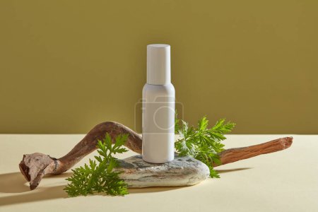 White plastic tube empty label on gray stone, mug-wort leaves and dry twig on brown background. Mockup for cosmetic of mug-wort extract - soften and moisturize skin, clean skin, prevent acne