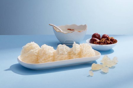 Photo for Raw bird's nest is placed on a long white plate, jujube, rock sugar and soup bowl decorated on blue background. Healthcare food, anti-aging, strengthen the immune system - Royalty Free Image