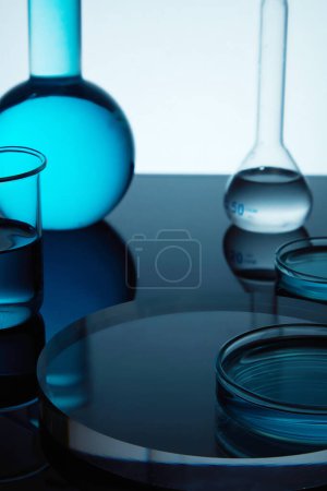 Téléchargez les photos : Fond d'art minimal avec podium transparent, verrerie de laboratoire contenant du liquide bleu sur fond sombre. Thème du labo. Science et formation médicale - en image libre de droit