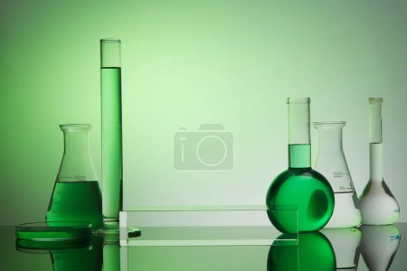 Front view of transparent empty podium, laboratory equipment - test tube, boiling flask, erlenmeyer flask and petri dish on green gradient background. Space for display product.