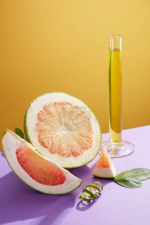 Front view of fresh pink pomelo slices, green leaves and test tube containing essence on yellow background. Scene for advertising cosmetics extracted from pink pomelo essential oils.