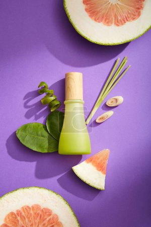 Photo for Top view of empty glass bottle, fresh pink pomelo slices, green leaves and lemongrass on purple background. Mockup scene for cosmetic product with natural essential oils. Copy space, flat lay. - Royalty Free Image