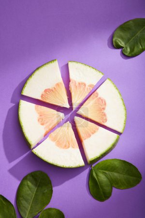 Photo for Minimal concept of pomelo with fresh pink pomelo slices cut into unique shapes and vivid green leaves on purple background. Top view, flat lay of scene advertising cosmetic of pomelo extract. - Royalty Free Image